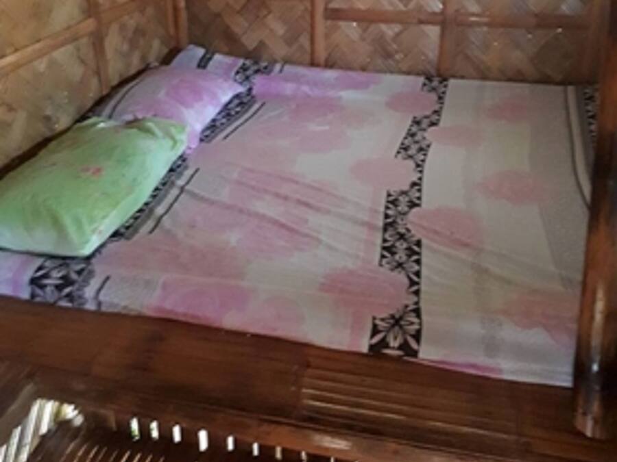 A wooden bed with a patterned bedspread and a green pillow in a room with bamboo walls and a window.