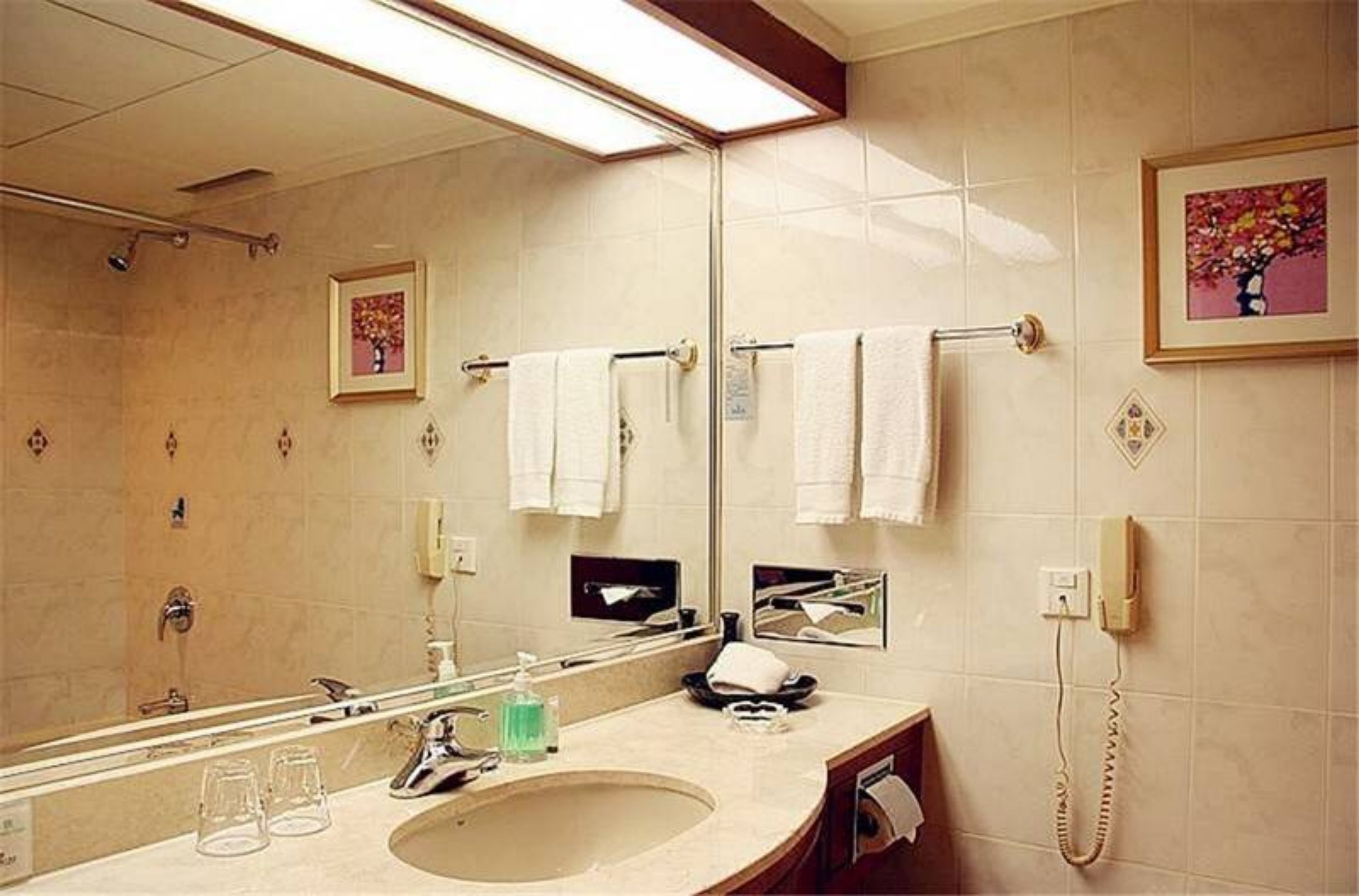 Un baño de hotel con un espejo grande, un lavamanos, un teléfono y varias toallas colgadas en un perchero.
