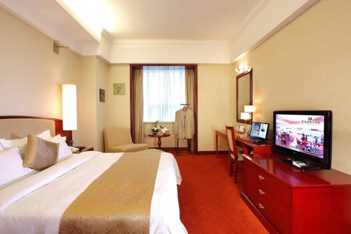 A hotel room with a bed, a desk with a computer, a television, and a window with curtains.