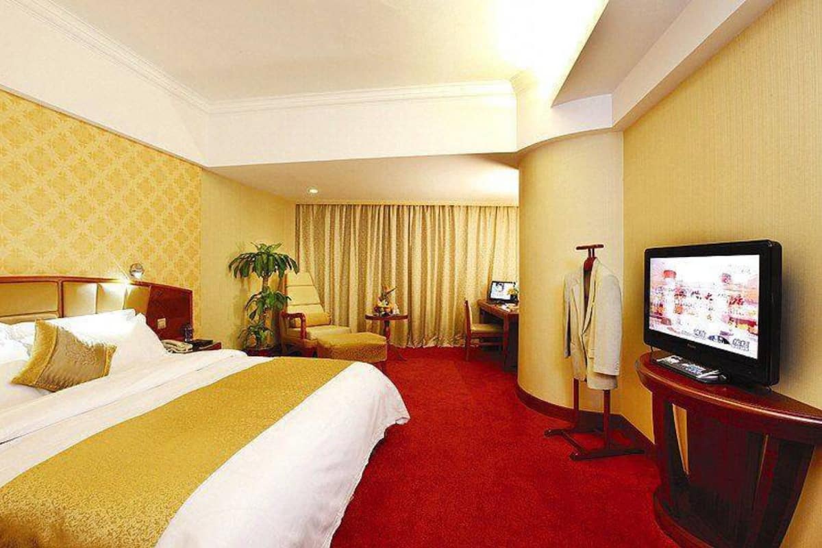 A hotel room with a large bed, a desk with a computer, a television, and a plant.