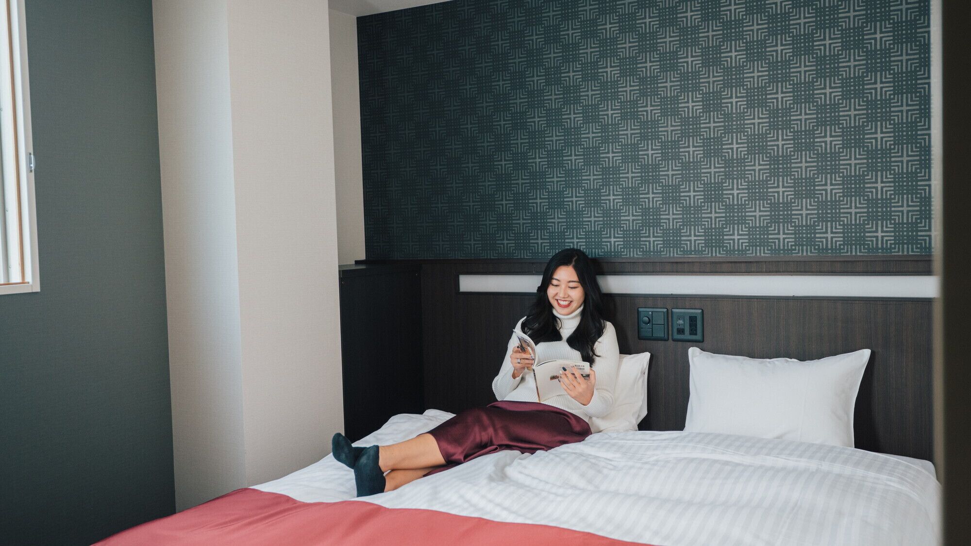 Hotellihuone, jossa on sänky, geometrisesti kuvioitu pääty, yöpöytä ja seinään asennettu ohjauspaneeli.