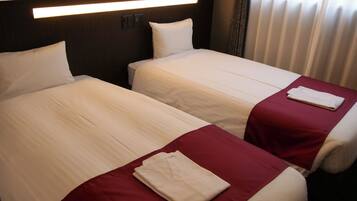 Zwei Betten mit weißer Bettwäsche und roten Überwürfen in einem Hotelzimmer.