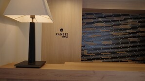 A reception desk with a lamp, a wooden panel wall, and a geometric patterned wall. - KANSEI Kyoto Hachijo (Kyoto)