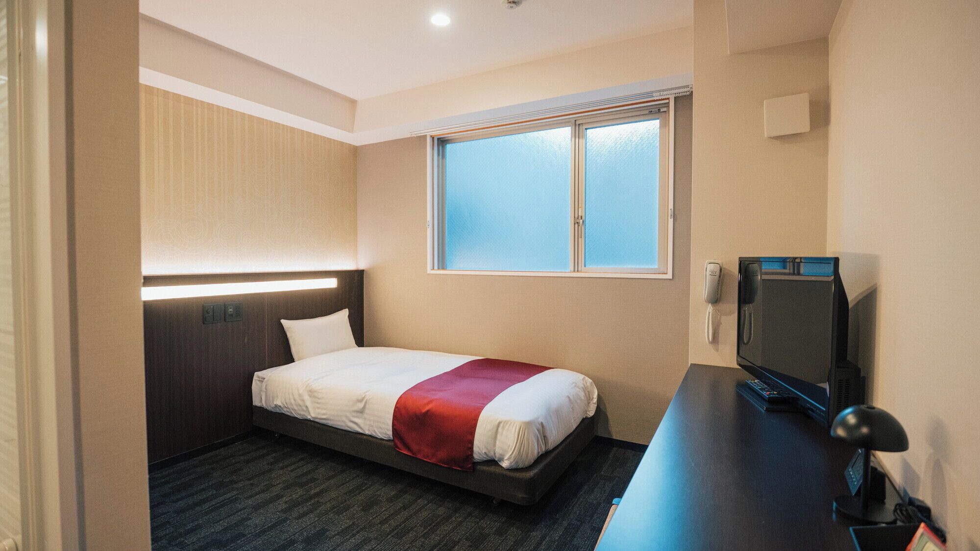 Een hotelkamer met een bed, een bureau met een televisie, een telefoon en een raam.