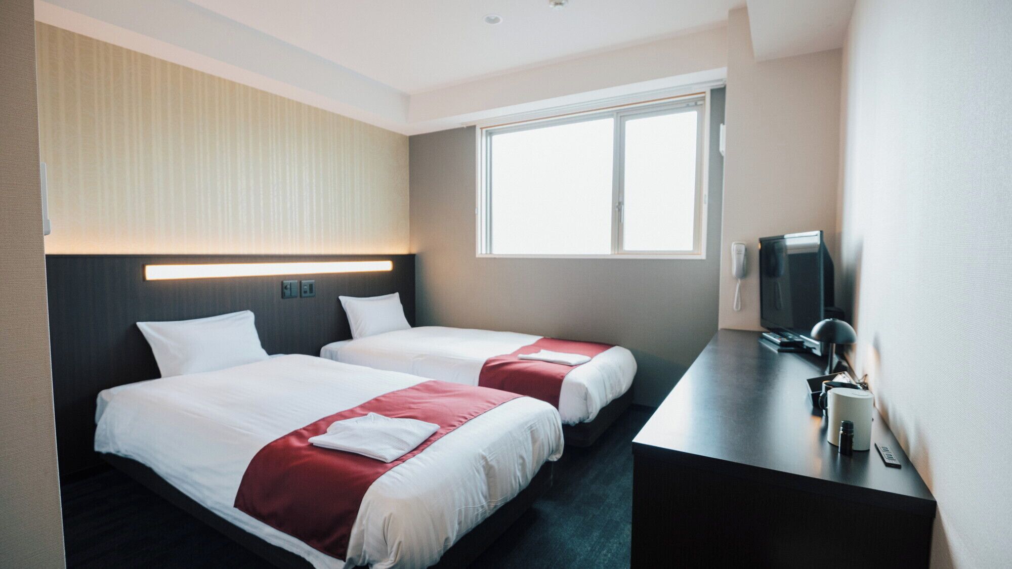 Een hotelkamer met twee bedden, een bureau met een computer, een televisie en een raam.
