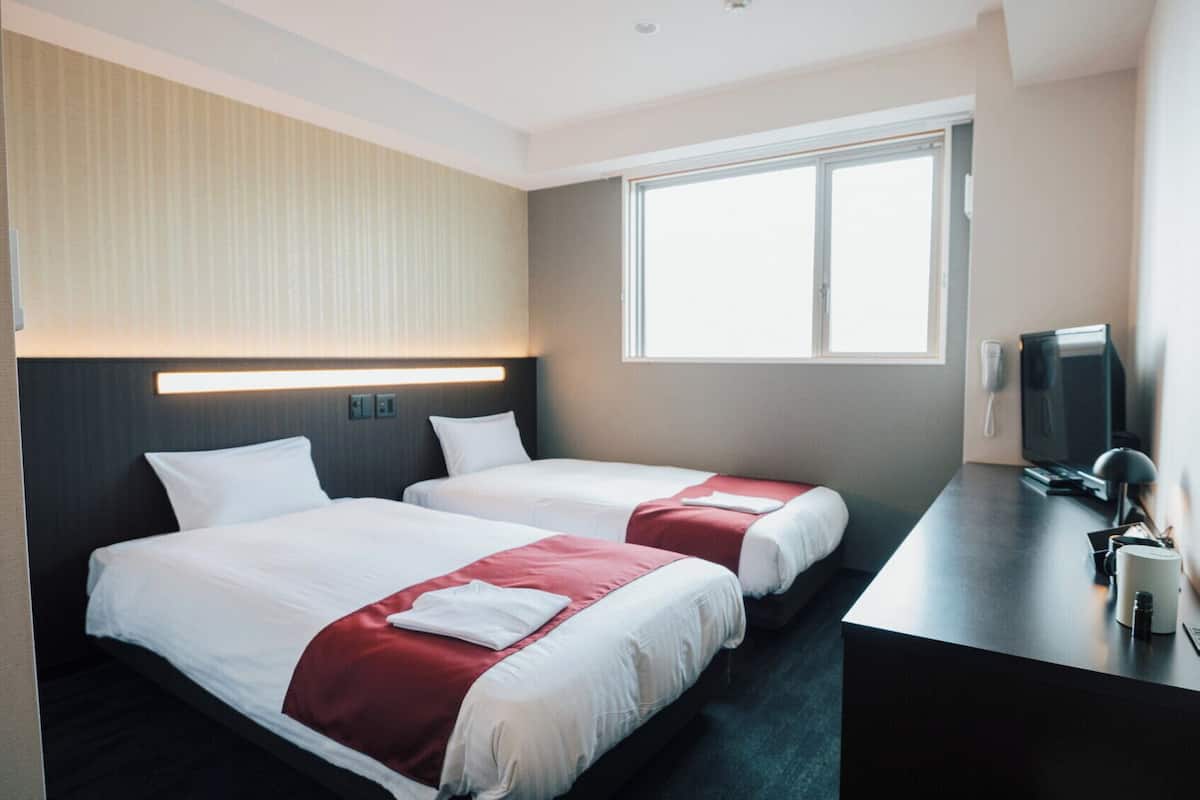 Ett hotellrum med två sängar, ett skrivbord med en dator, en tv och ett fönster.