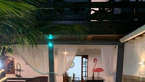 A cozy outdoor seating area with a round wicker sofa, a dining table, and a pool. - Flamingo Beach Pousada (Cabo Frio)