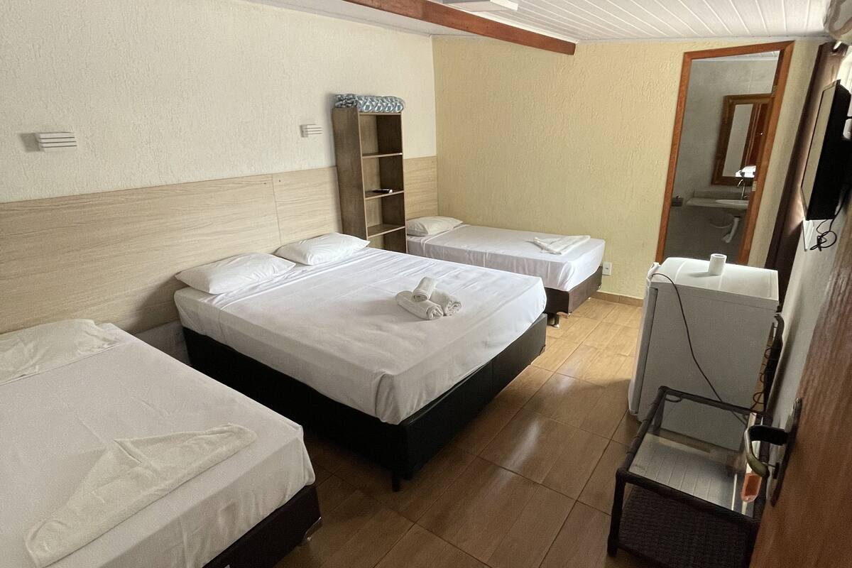 Ein Hotelzimmer mit drei Einzelbetten, einem Holzschrank, einem kleinen Schreibtisch mit Stuhl und einem Spiegel an der Wand.