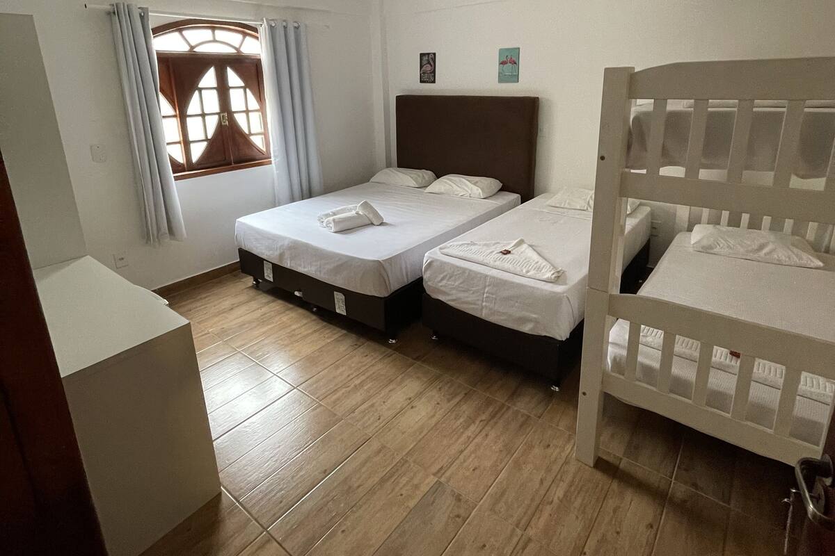 Ein Schlafzimmer mit zwei Betten, einem Fenster mit Vorhängen, einem Holzboden und einer Deckenleuchte.