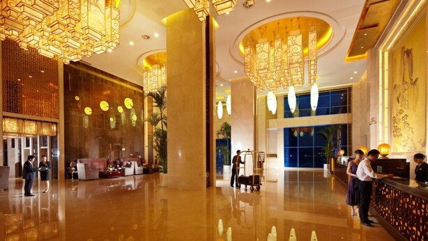 A spacious lobby with high ceilings, ornate chandeliers, and a reception area with staff.