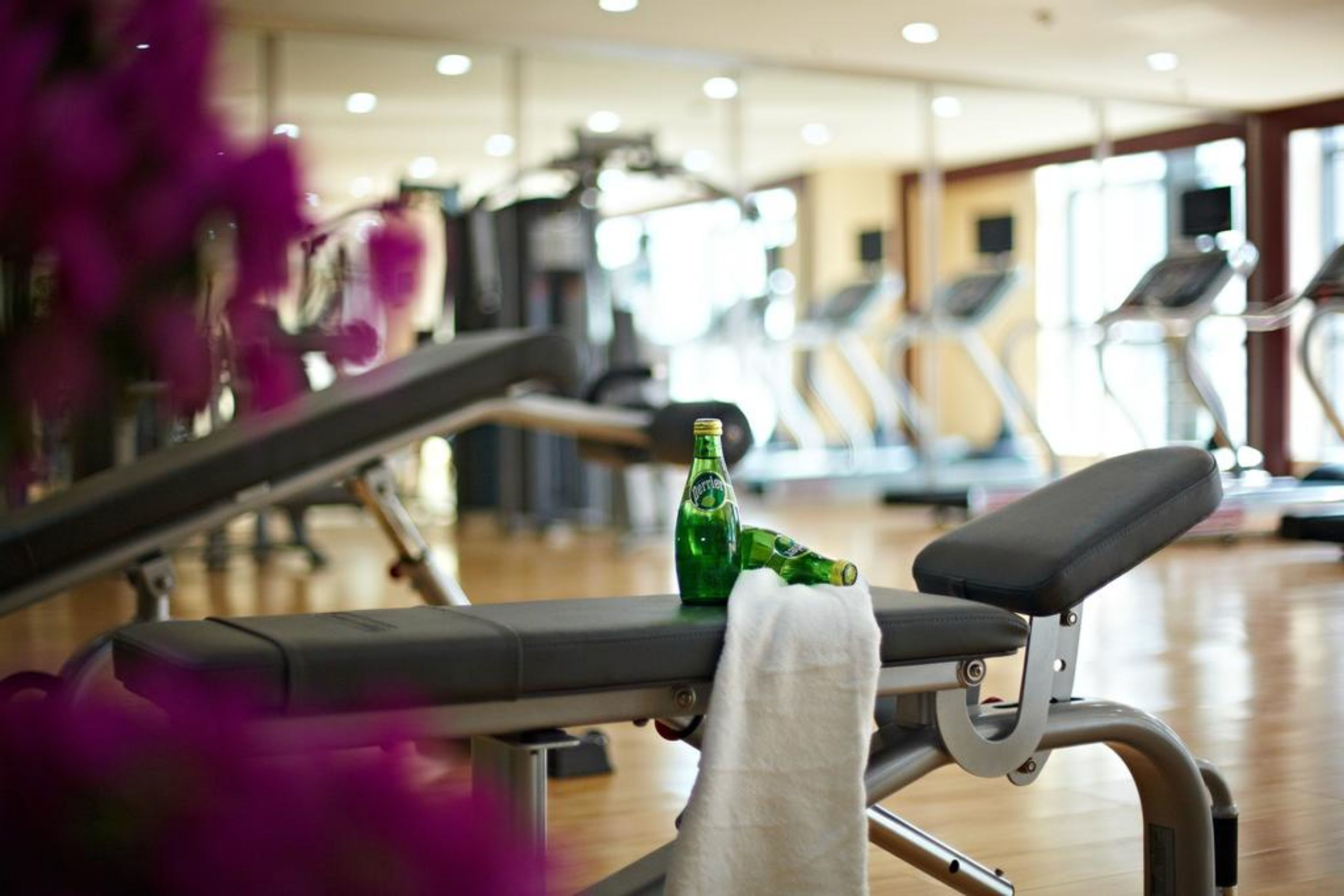A gym with exercise equipment, a bench, and a bottle of beer on the bench.