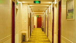 A hotel hallway with a patterned carpet, doors, and a green exit sign. - Yuehang Hotel (Zhuhai)