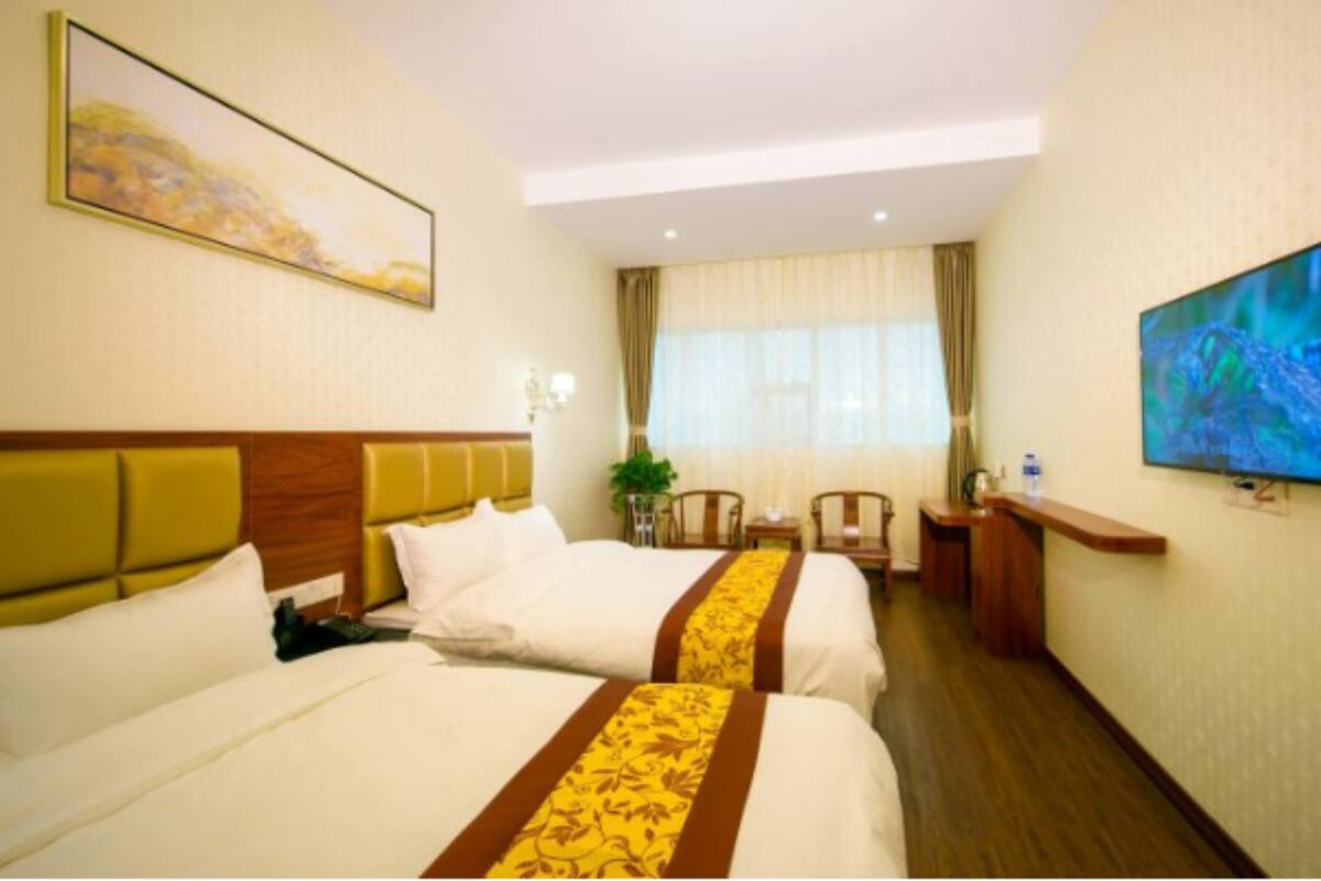A hotel room with two beds, a television, a desk, and a window with curtains.