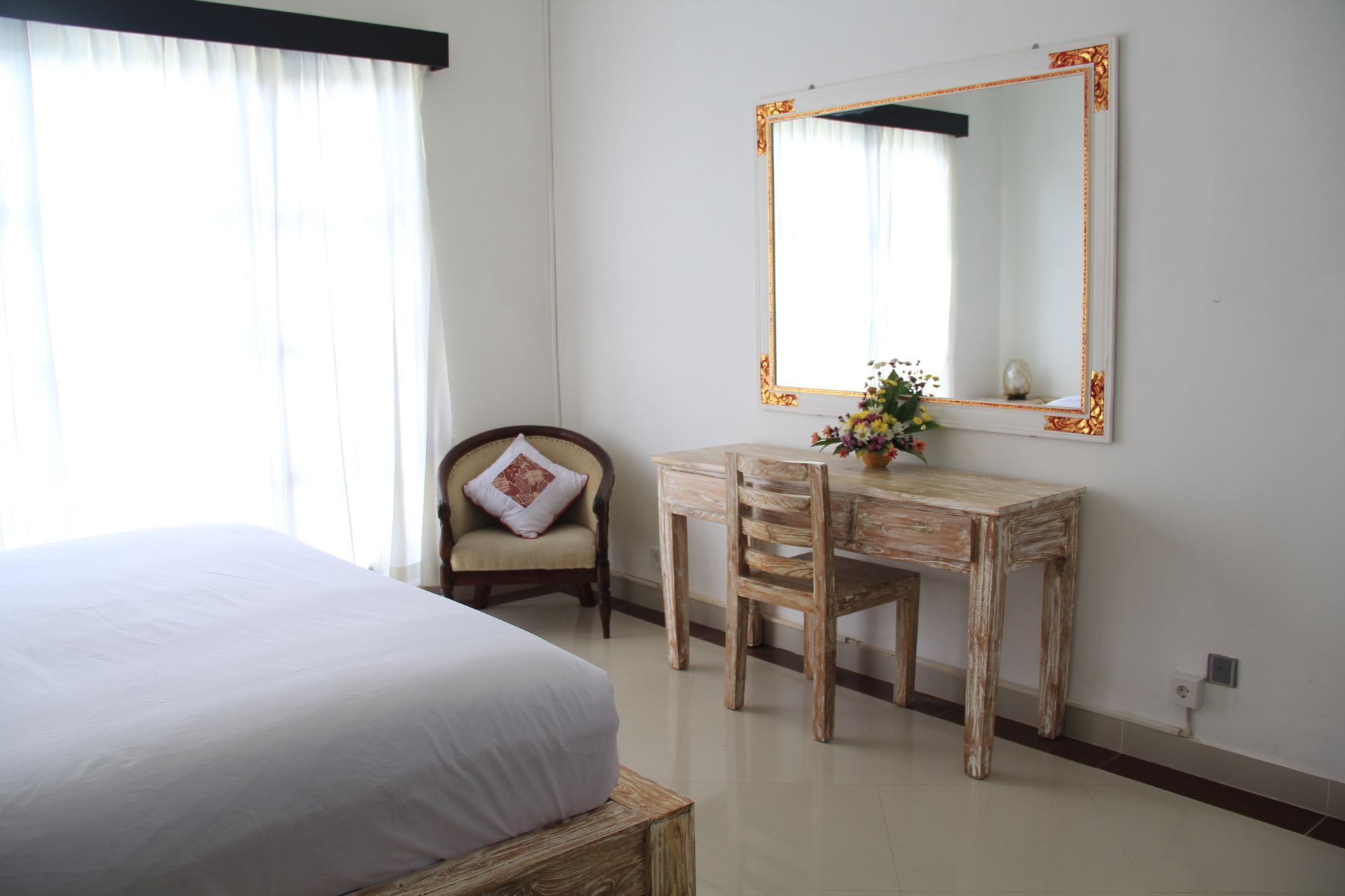 A bedroom with a bed, a wooden desk, a chair, and a large mirror on the wall.
