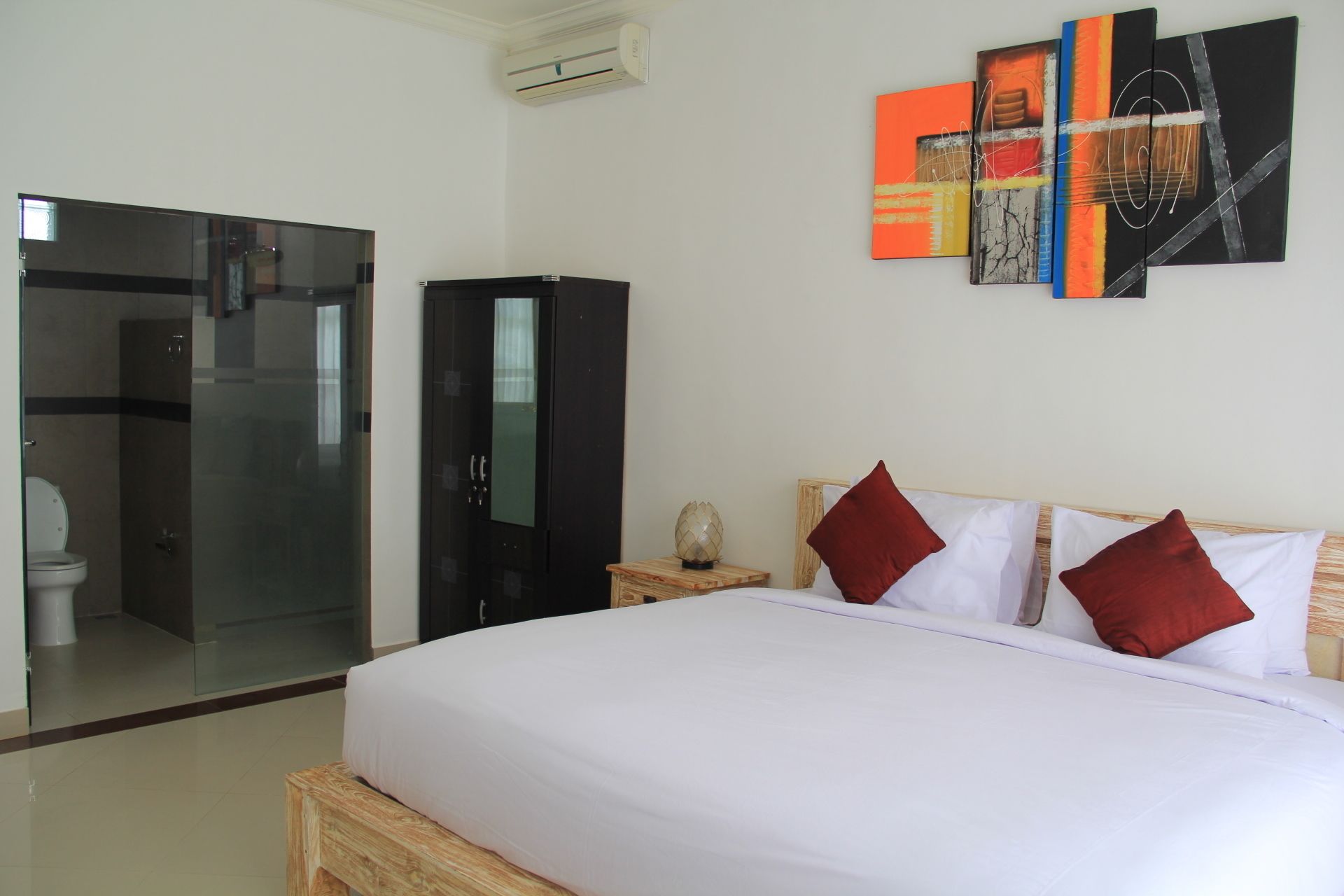 Une chambre d’hôtel comprenant un lit, une armoire, une douche en verre et un mur orné d’œuvres d’art abstraites.