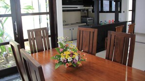 Un comedor con una mesa y sillas de madera, un jarrón con flores y una cocina al fondo.