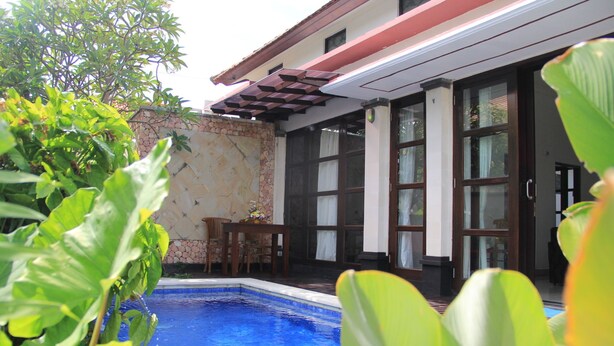 Zona de piscina con pared de piedra, muelle de madera y mesa con sillas.