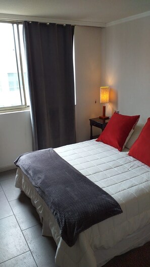 Ein Hotelzimmer mit Bett, Nachttisch mit Lampe und einem Fenster mit Vorhängen.