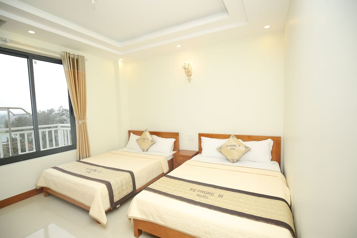 Habitación de hotel con dos camas, una ventana con cortinas, una lámpara de pared y vista al balcón.