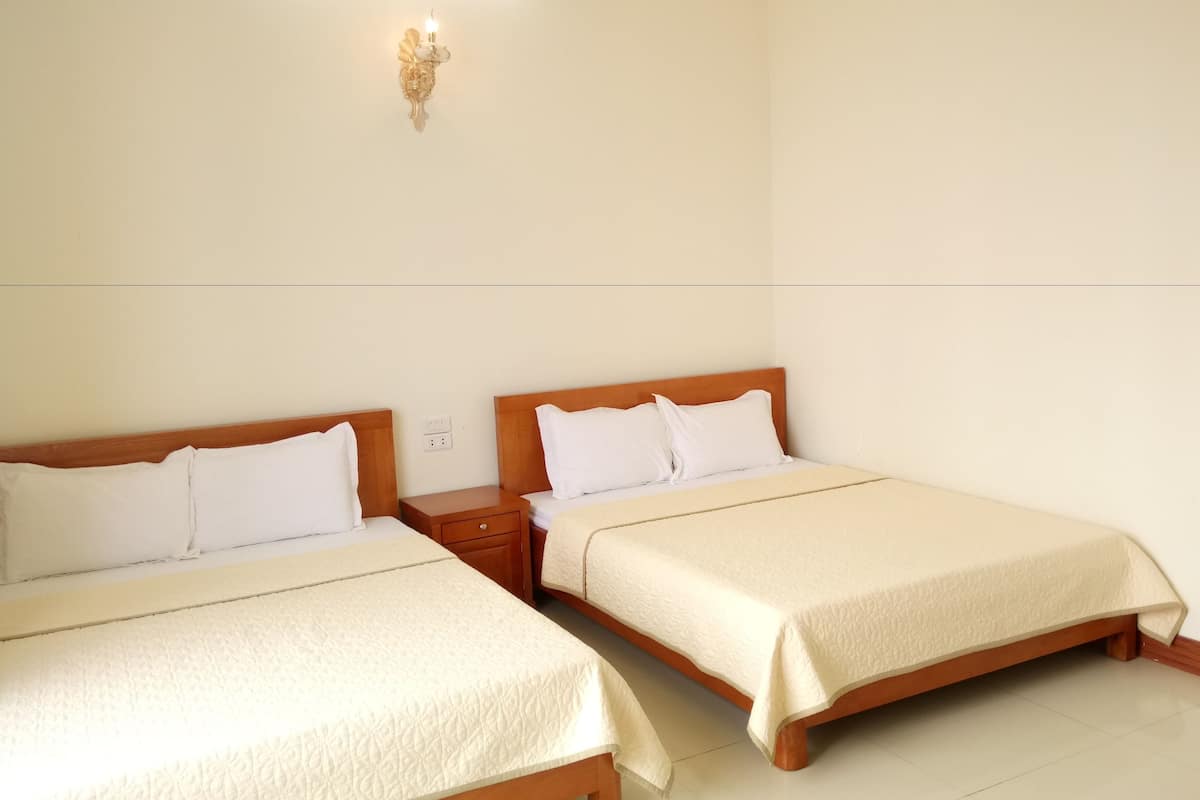 Dos camas individuales con cabeceros de madera, ropa de cama blanca y una lámpara fijada a la pared.