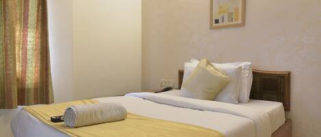A neatly made bed with a yellow blanket, white pillows, and a remote control on the bed.