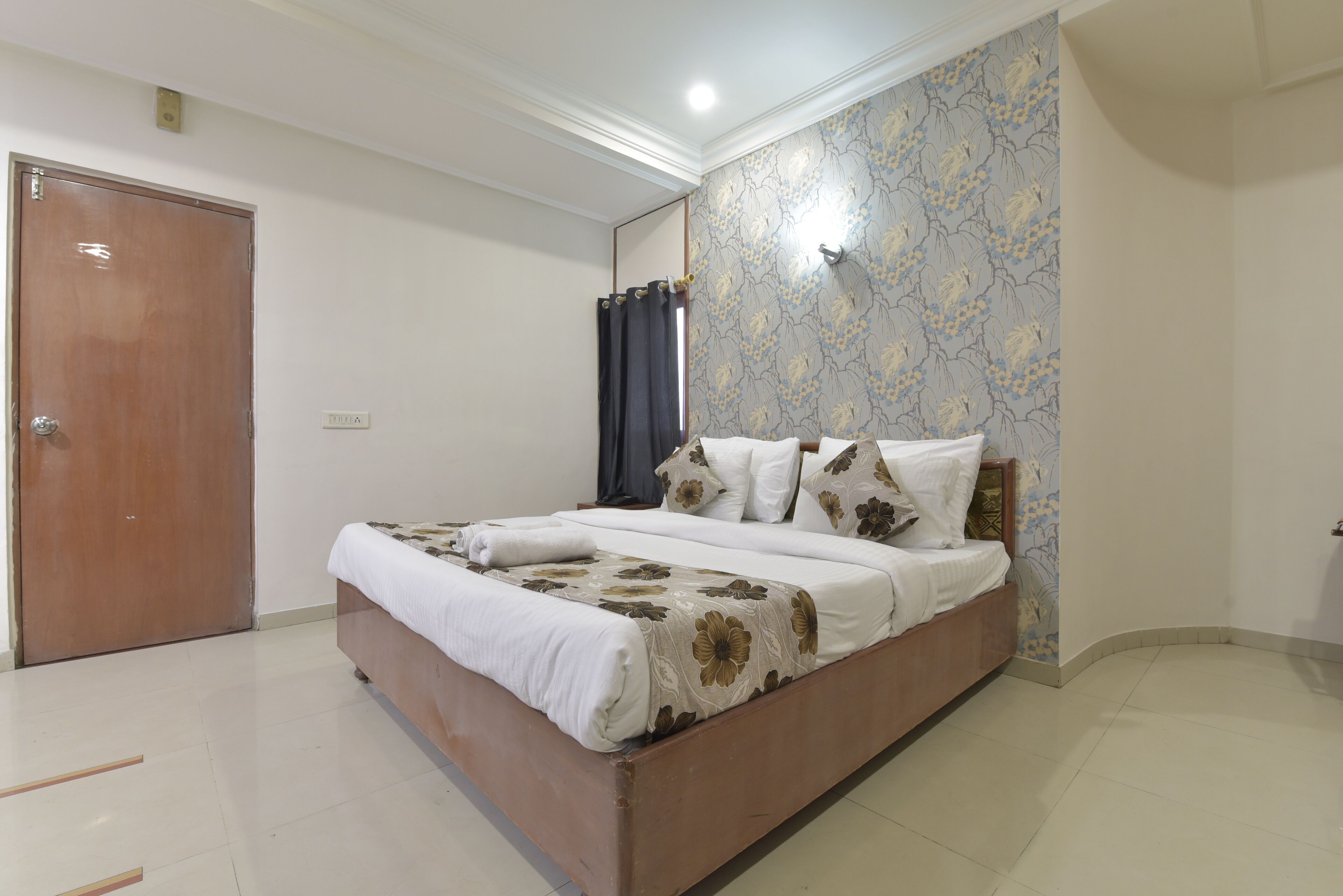 A bedroom with a wooden bed, white bedding, a floral-patterned wall, and a closed door.