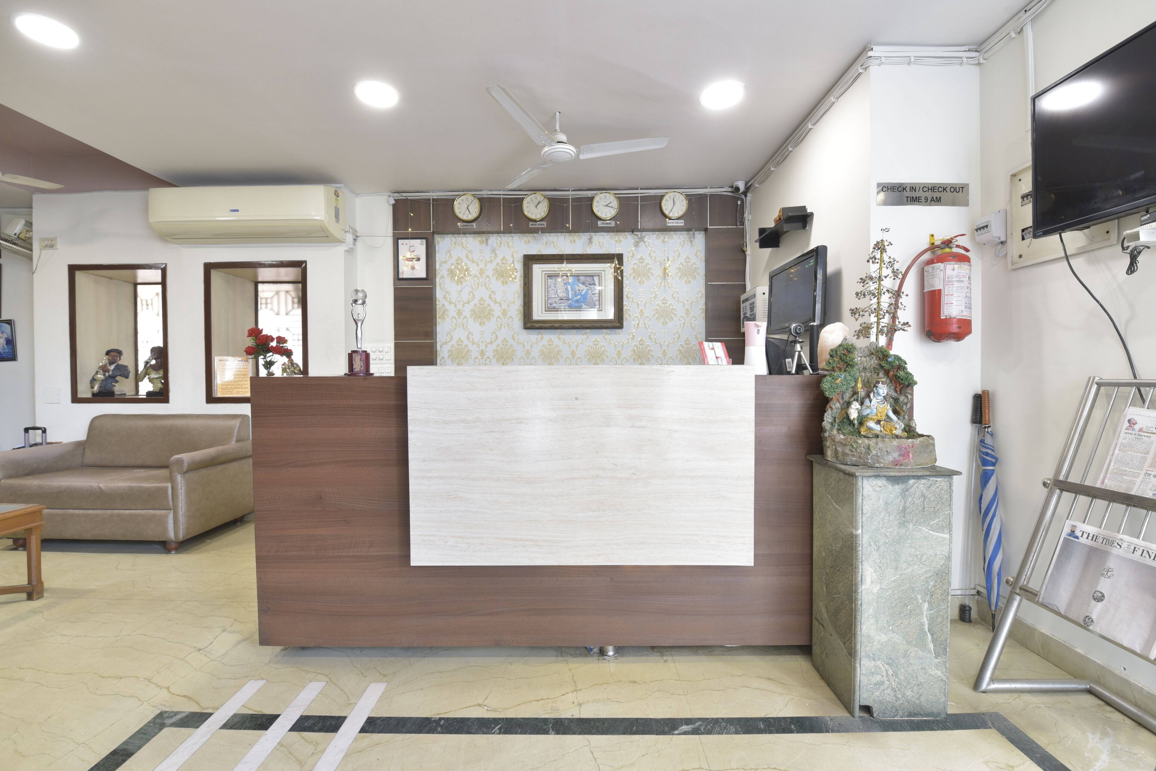 A reception area with a wooden reception desk, a ceiling fan, a fire extinguisher, a clock, and a television on the wall.