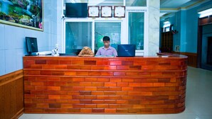 A reception desk with a person seated behind it, a large painting on the wall, and three clocks above the desk. - Co Cuc Hotel - Hostel (Phong Nha)