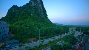 A mountain with dense green vegetation, a curved road, and buildings in the foreground. - Co Cuc Hotel - Hostel (Phong Nha)