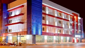 A multi-story hotel with balconies, a prominent blue-lit tower, and a ground-level restaurant. - Tyche Boutique Hotel (Legazpi)