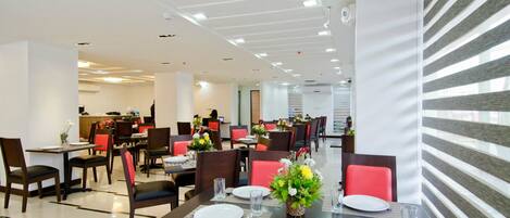 A modern dining area with multiple tables and chairs, some with red cushions.