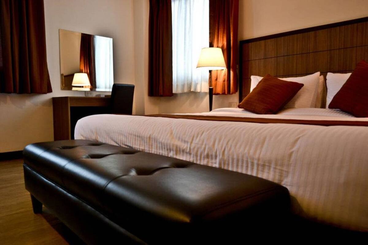 A hotel room with a large bed, a nightstand, a desk, a chair, a mirror, and a window with curtains.