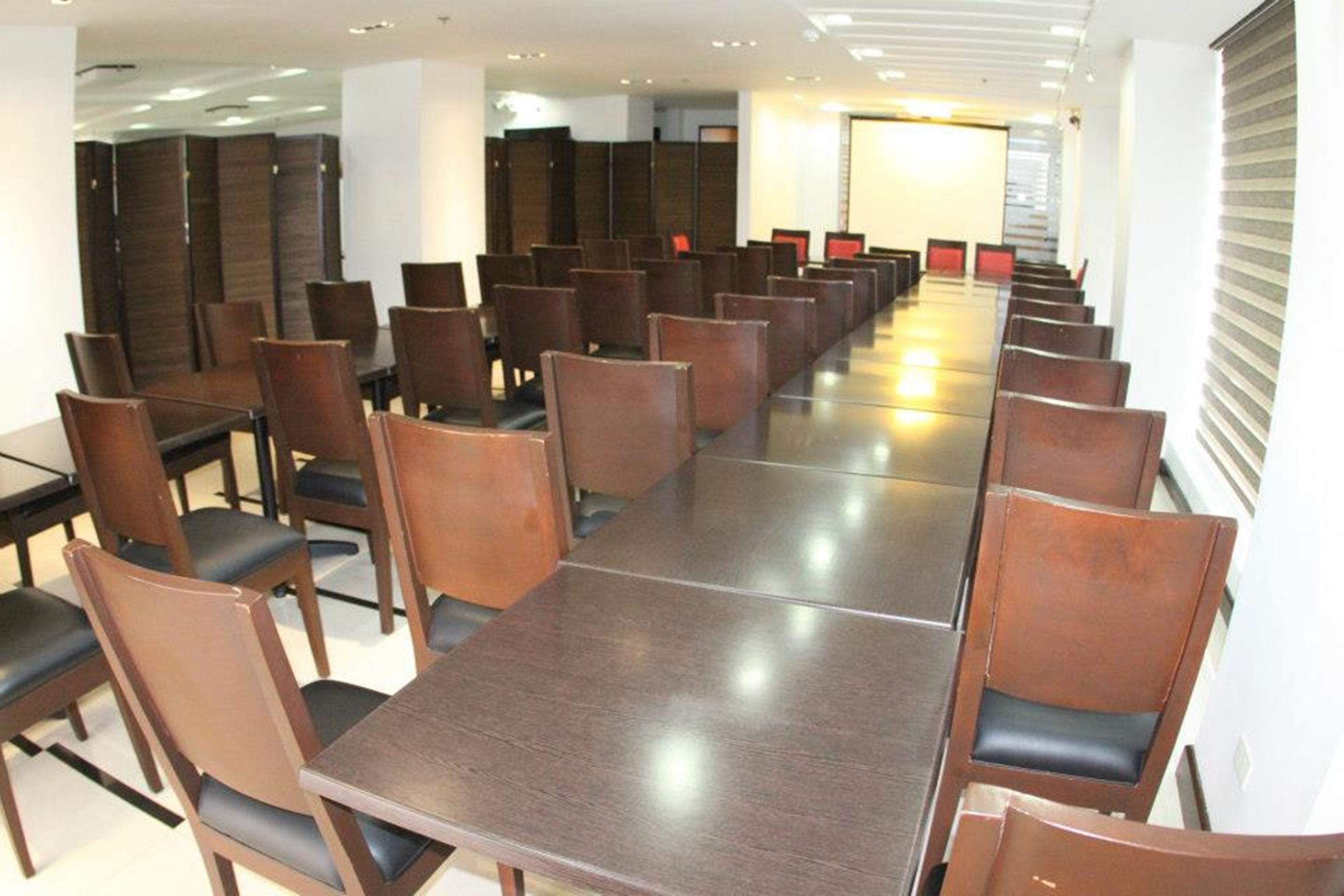 Un salón de conferencias con largas mesas y sillas, separado por paneles de madera.