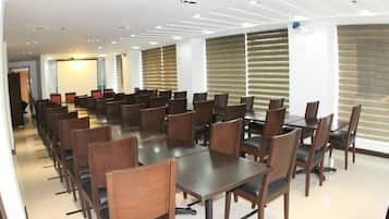 Sala de conferências com várias mesas e cadeiras, amplas janelas com persianas e design de teto moderno.