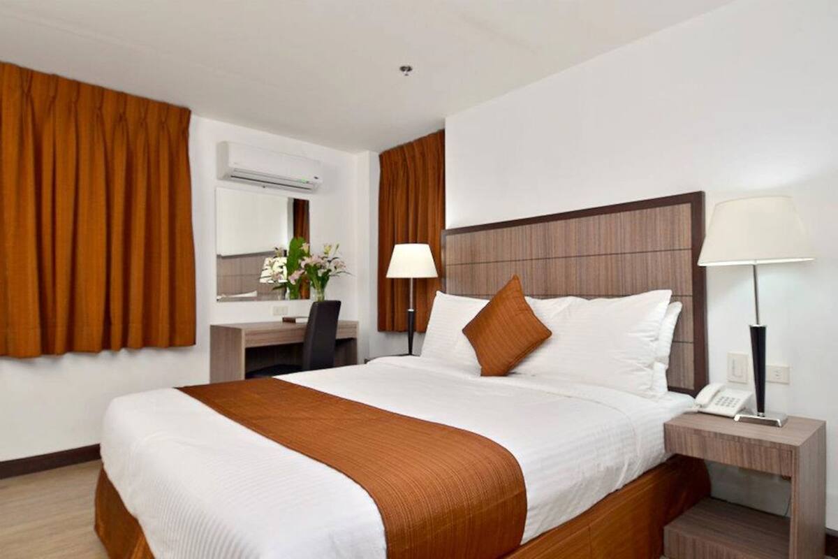 A hotel room with a large bed, a desk, a chair, a lamp, and a phone on the nightstand.
