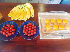 A wooden table with two bowls of strawberries and bananas, and a plastic container with sliced oranges.