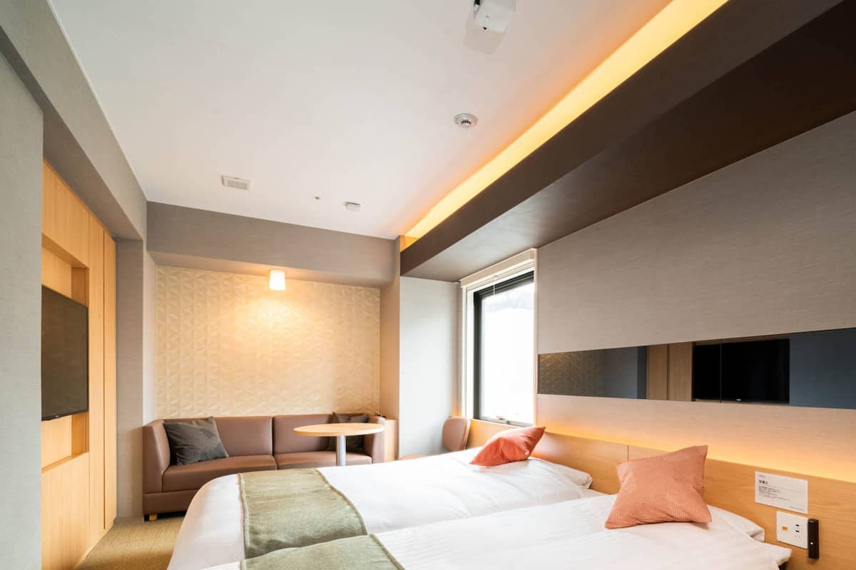 Una habitación de hotel moderna con una cama grande, un sofá, una mesita y un televisor montado en la pared.
