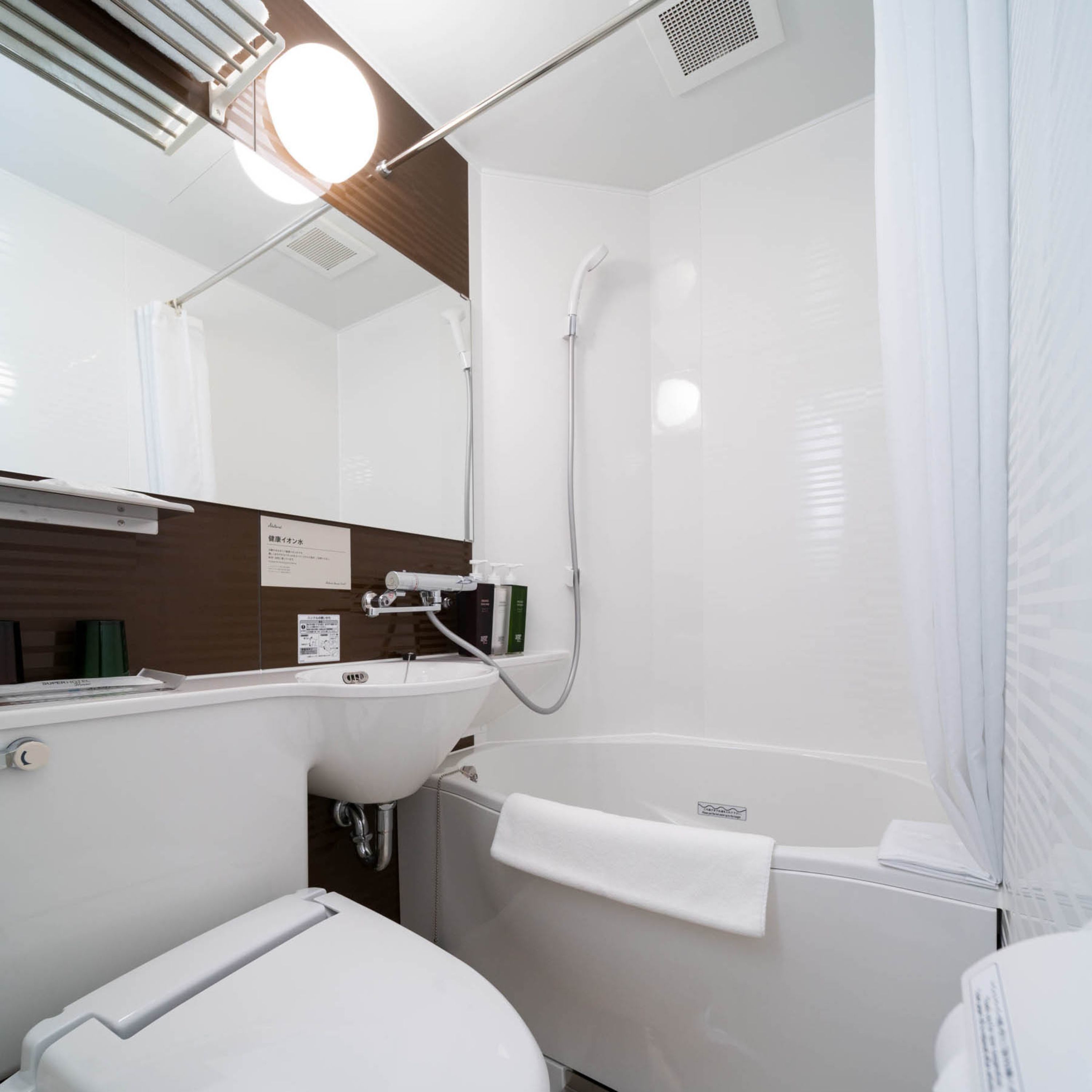 Un baño moderno con lavamanos, inodoro y bañera blancos. Hay un cabezal de ducha y una toalla colgada en la pared.