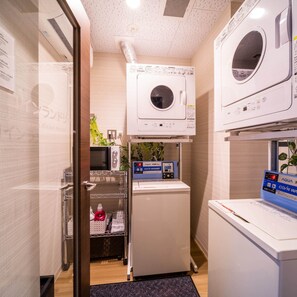 A compact laundry room with a front-loading washer and dryer, a small refrigerator, and a shelf with cleaning supplies.