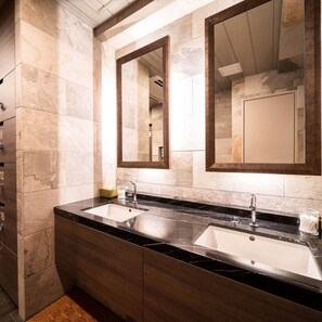 A modern bathroom with two sinks, marble tiles, wooden cabinetry, and large mirrors.