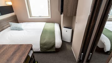Una habitación compacta con cama, mesita de noche, escritorio pequeño, ventana, televisor montado en la pared y armario.