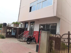 A building with a staircase leading to a door marked C-237, a motorcycle parked in front, and a gated entrance.