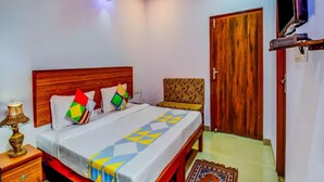 A bedroom with a wooden bed, a ceiling fan, a TV mounted on the wall, and a door. - Airport Sky Inn (Jaipur)