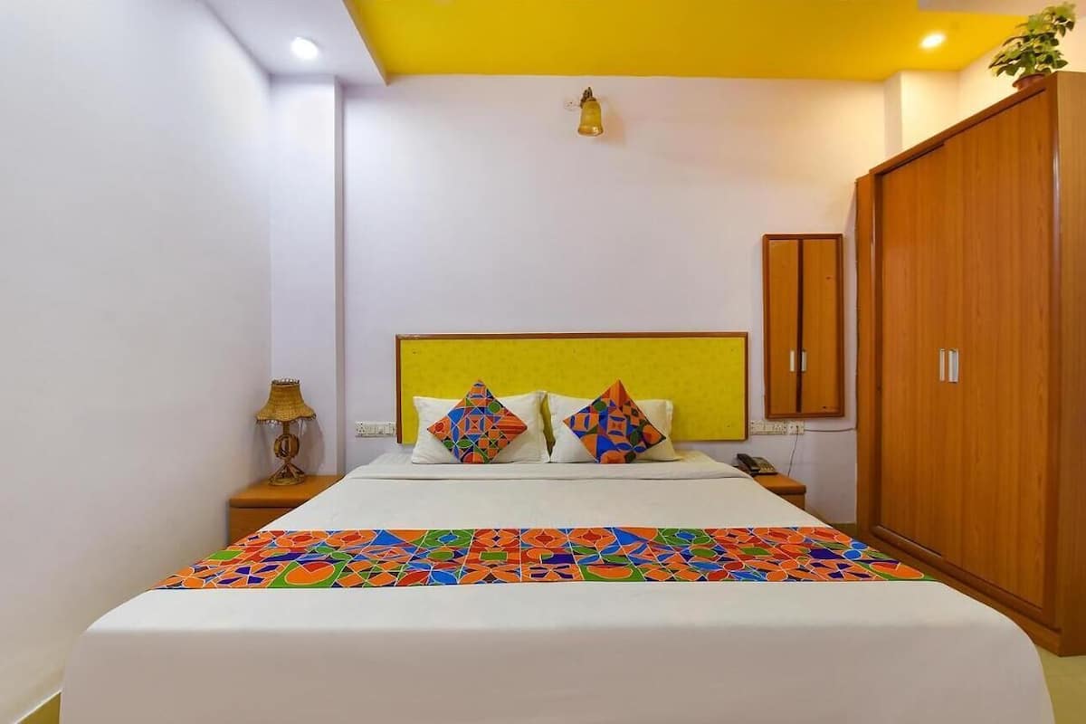 Una habitación de hotel con cama, mesita de noche, lámpara, armario y una lámpara fijada a la pared.