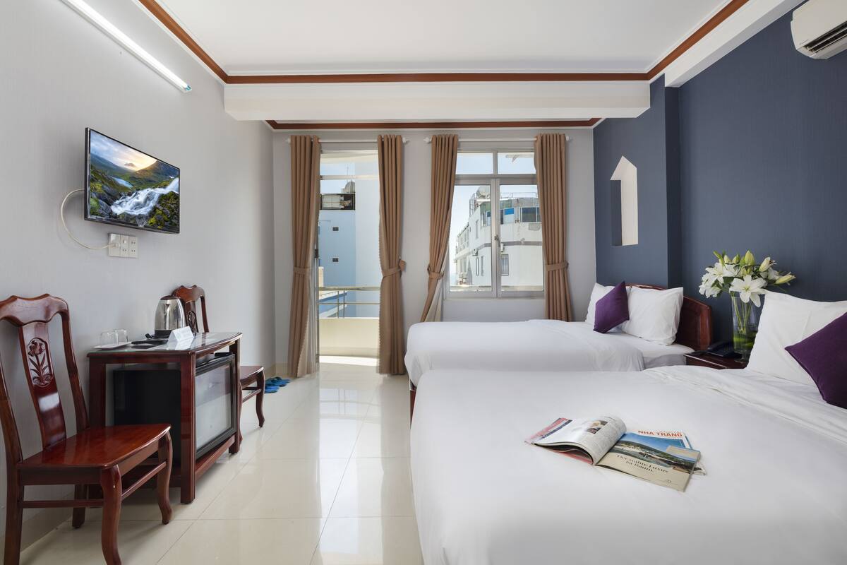 Une chambre d’hôtel avec deux lits, une télévision, un bureau avec une chaise et une vue sur le balcon extérieur.