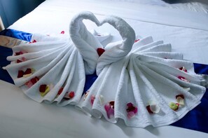Una cama con una toalla blanca dispuesta en forma de cisne, decorada con pétalos de rosa.
