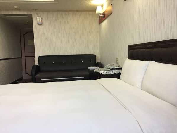 A hotel room with a bed, a small desk with a telephone, a sofa, and a wall-mounted lamp. - King Lo Tung Hotel (Luodong)