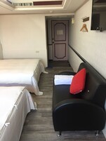 Habitación de hotel con dos camas, un sofá negro y una almohada roja, además de un perchero de madera.