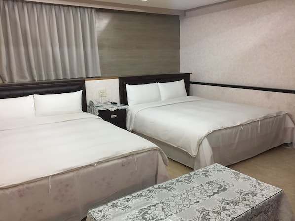 Habitación de hotel con dos camas, una mesita de noche con teléfono y lámpara, y una pequeña mesa con mantel estampado.