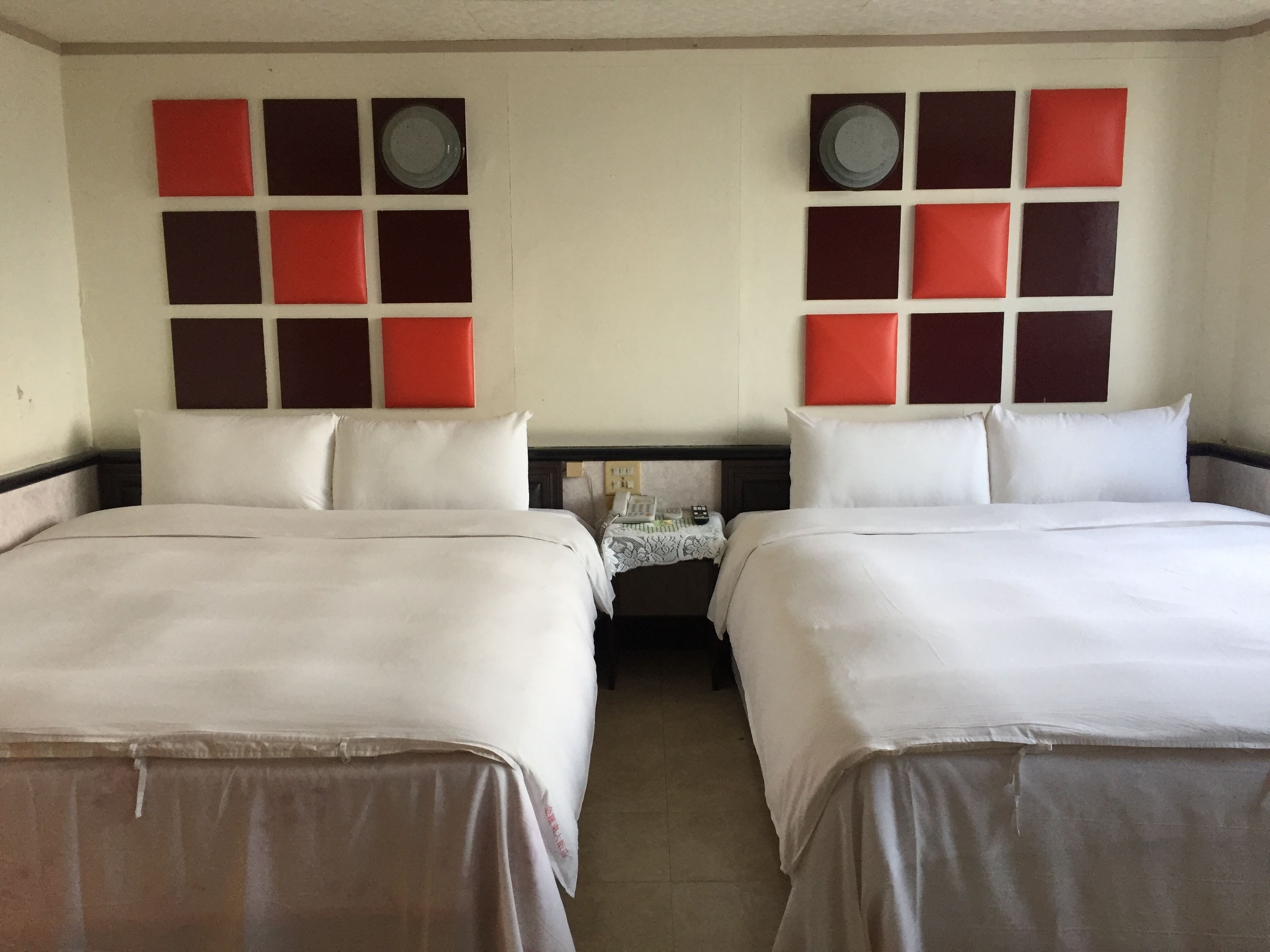 A hotel room with two beds, a nightstand, and a wall with a red and black pattern.